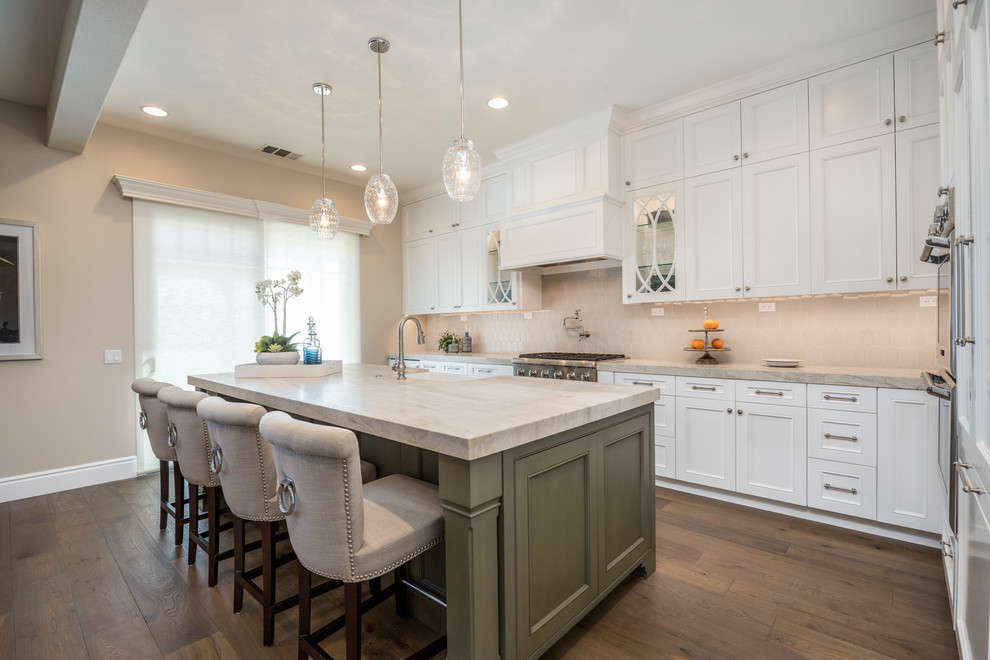 Inspiration for a mid-sized traditional l-shaped open plan kitchen in Orange County with a farmhouse sink, recessed-panel cabinets, grey splashback, ceramic splashback, panelled appliances, medium hardwood floors, with island, brown floor and beige benchtop.