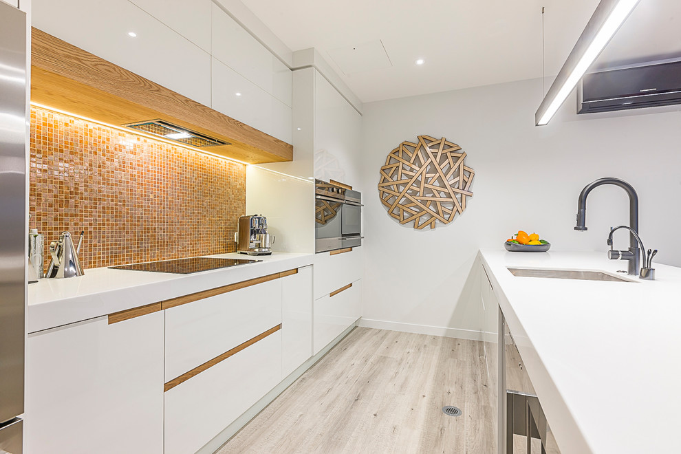 Photo of a mid-sized contemporary galley eat-in kitchen in Auckland with an undermount sink, white cabinets, orange splashback, mosaic tile splashback, stainless steel appliances, flat-panel cabinets, solid surface benchtops, light hardwood floors, a peninsula and multi-coloured floor.