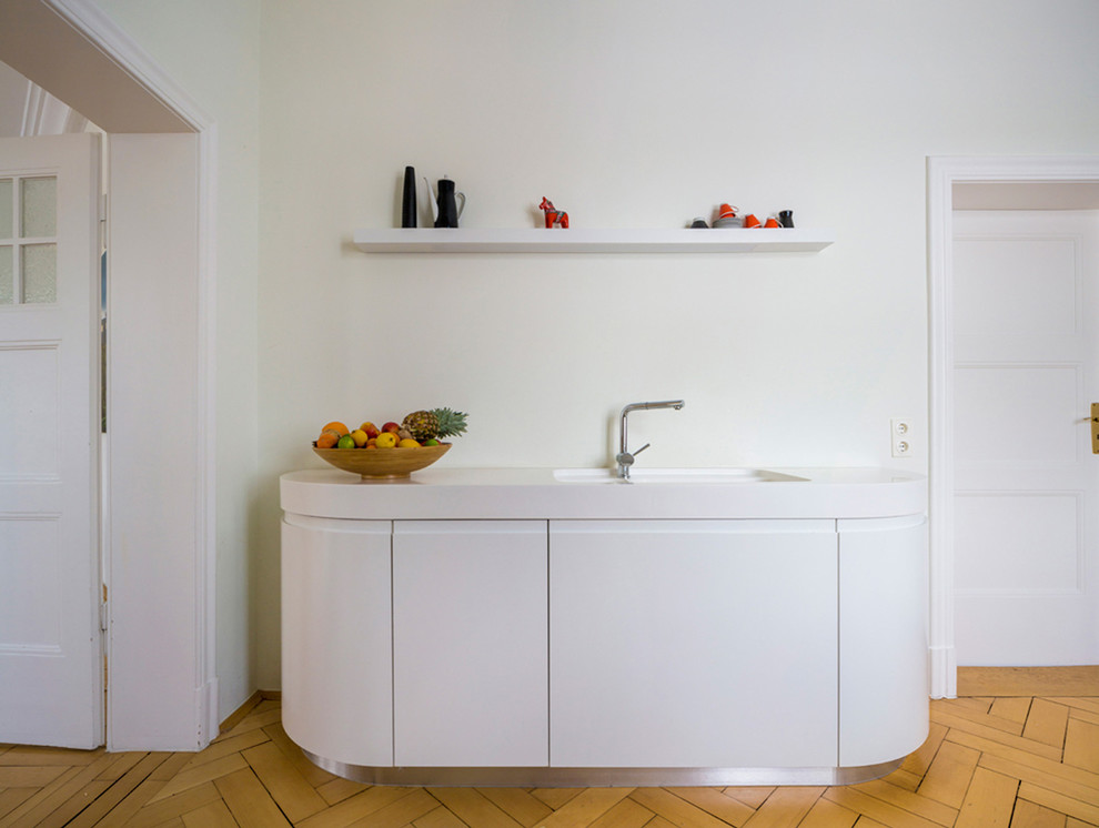 This is an example of a contemporary single-wall kitchen in Leipzig with an undermount sink, flat-panel cabinets, white cabinets and light hardwood floors.