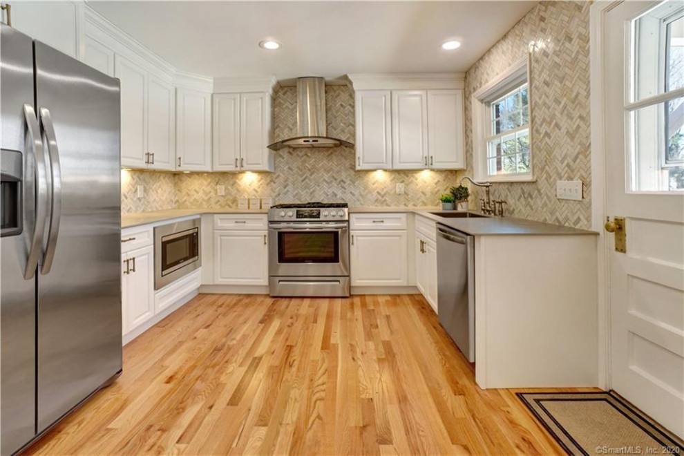 Mid-sized transitional l-shaped light wood floor eat-in kitchen photo with an undermount sink, shaker cabinets, white cabinets, marble backsplash, stainless steel appliances and gray countertops