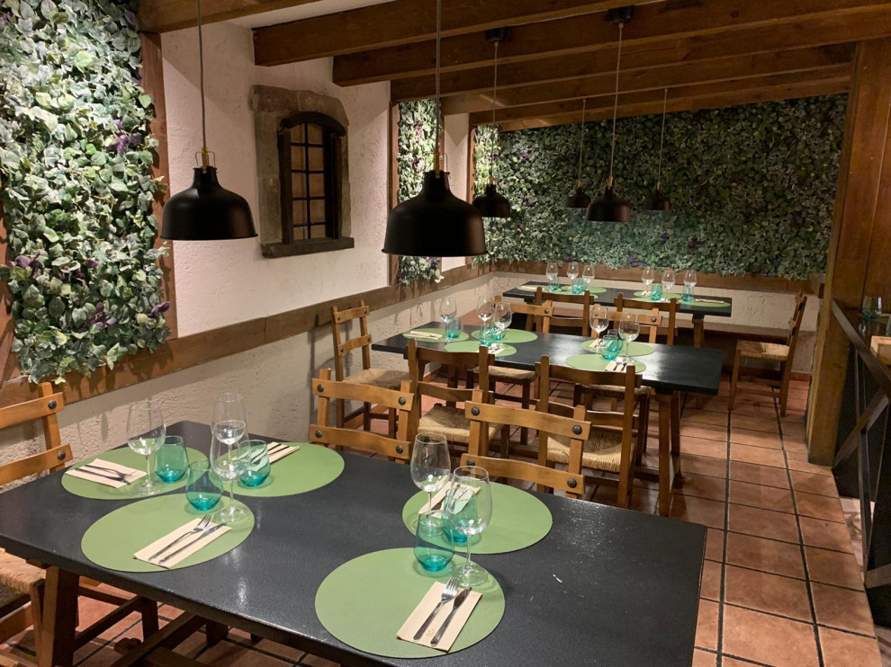 Modelo de comedor rural de tamaño medio abierto con paredes blancas, suelo de baldosas de cerámica, chimenea de esquina, marco de chimenea de piedra, suelo beige, vigas vistas y madera