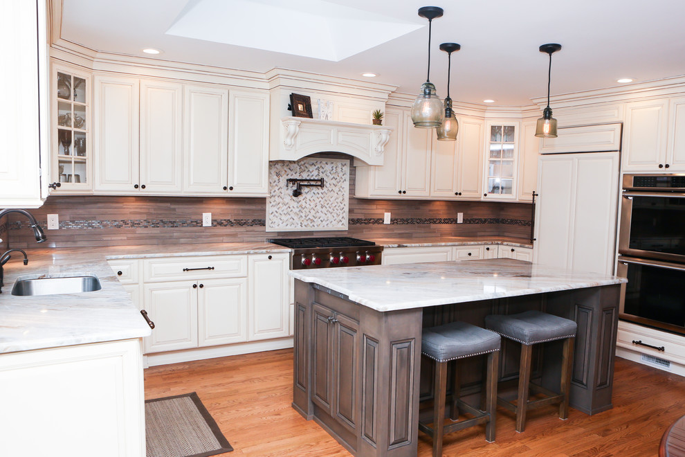 Large transitional u-shaped light wood floor eat-in kitchen photo in Newark with an undermount sink, raised-panel cabinets, distressed cabinets, granite countertops, brown backsplash, mosaic tile backsplash, stainless steel appliances and an island