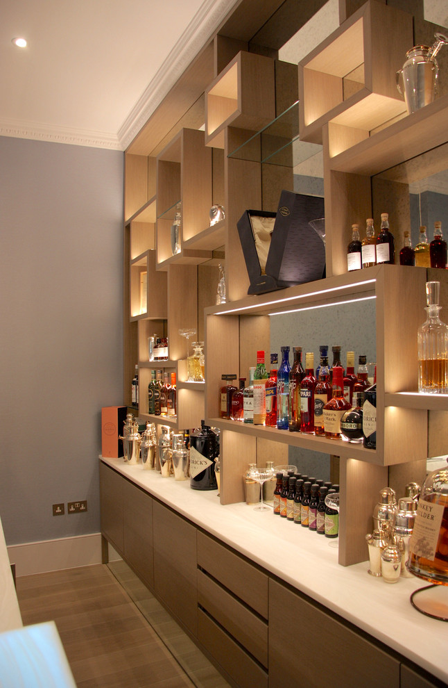 Large modern single-wall bar cart in London with a drop-in sink, open cabinets, light wood cabinets, onyx benchtops, multi-coloured splashback, mirror splashback, light hardwood floors, grey floor and white benchtop.