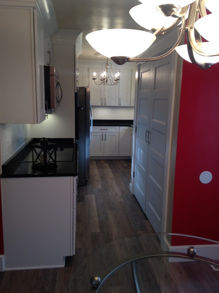 Mid-sized arts and crafts u-shaped vinyl floor home design photo with a double-bowl sink, shaker cabinets, white cabinets, quartz countertops, white backsplash, porcelain backsplash, stainless steel appliances and no island