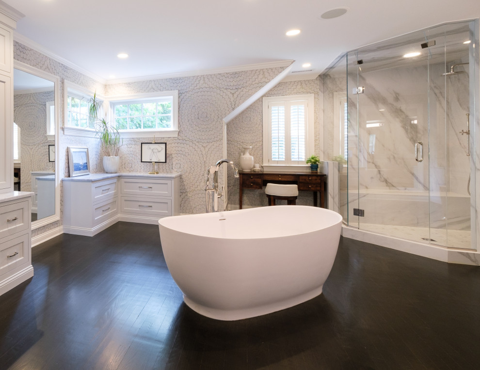 Inspiration for an expansive transitional master bathroom in New York with recessed-panel cabinets, grey cabinets, a freestanding tub, a double shower, multi-coloured walls, dark hardwood floors, an undermount sink, marble benchtops, a hinged shower door, blue benchtops, an enclosed toilet, a double vanity, a built-in vanity and wallpaper.