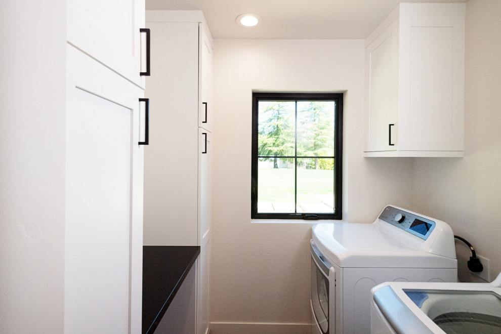 This is an example of a large country l-shaped laundry room in Sacramento with an undermount sink, shaker cabinets, black cabinets, quartz benchtops, white splashback, subway tile splashback, light hardwood floors, brown floor, black benchtop and vaulted.