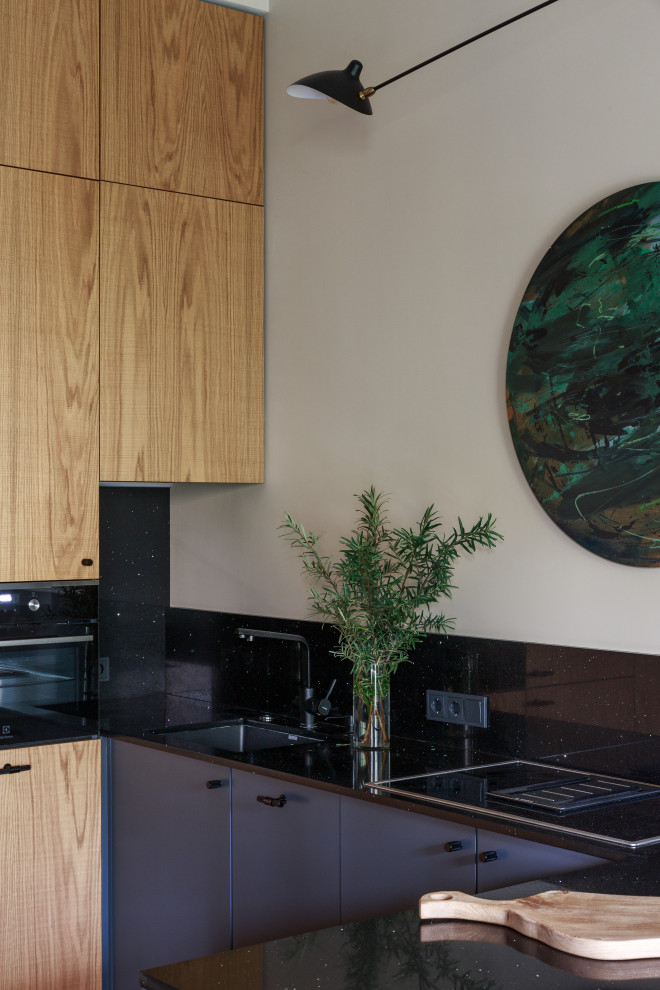Cette photo montre une cuisine américaine bicolore tendance avec une crédence noire, îlot, plan de travail noir, un placard à porte plane et des portes de placard grises.