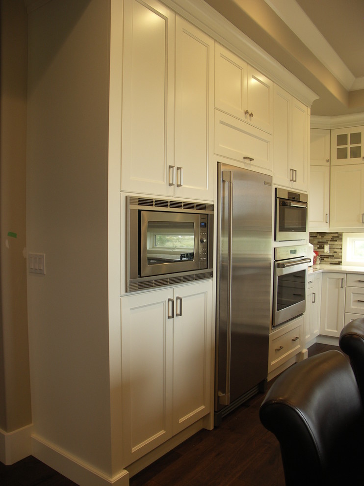 Example of a transitional u-shaped medium tone wood floor kitchen design in Edmonton with a farmhouse sink, recessed-panel cabinets, white cabinets, glass tile backsplash, stainless steel appliances and an island