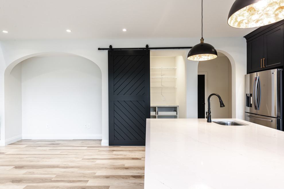 Mid-sized transitional l-shaped laminate floor and brown floor eat-in kitchen photo in Toronto with an undermount sink, recessed-panel cabinets, black cabinets, quartz countertops, white backsplash, ceramic backsplash, stainless steel appliances, an island and white countertops