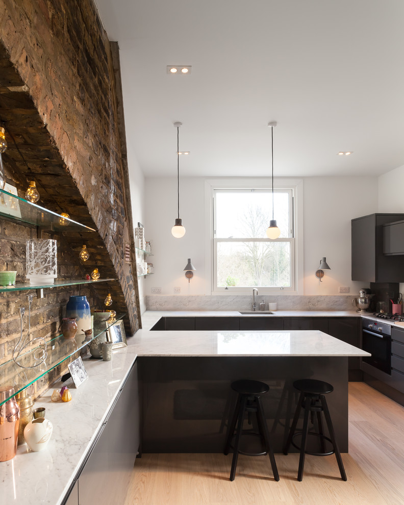 Photo of a mid-sized contemporary kitchen in London with an undermount sink, flat-panel cabinets, black cabinets, marble benchtops, light hardwood floors, a peninsula and beige floor.