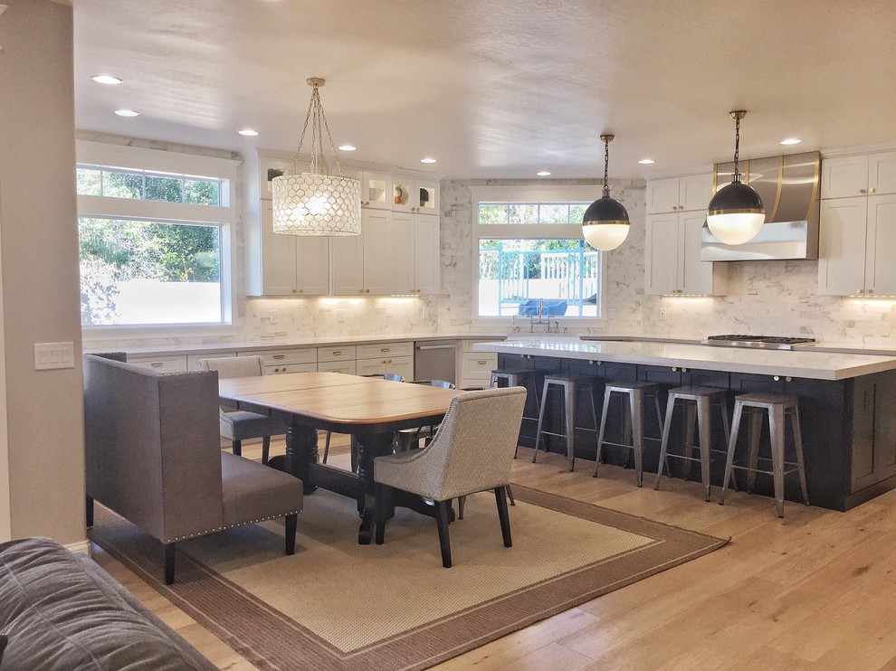 Large transitional l-shaped eat-in kitchen in Phoenix with a farmhouse sink, shaker cabinets, white cabinets, quartz benchtops, white splashback, marble splashback, stainless steel appliances, laminate floors, with island, beige floor and white benchtop.