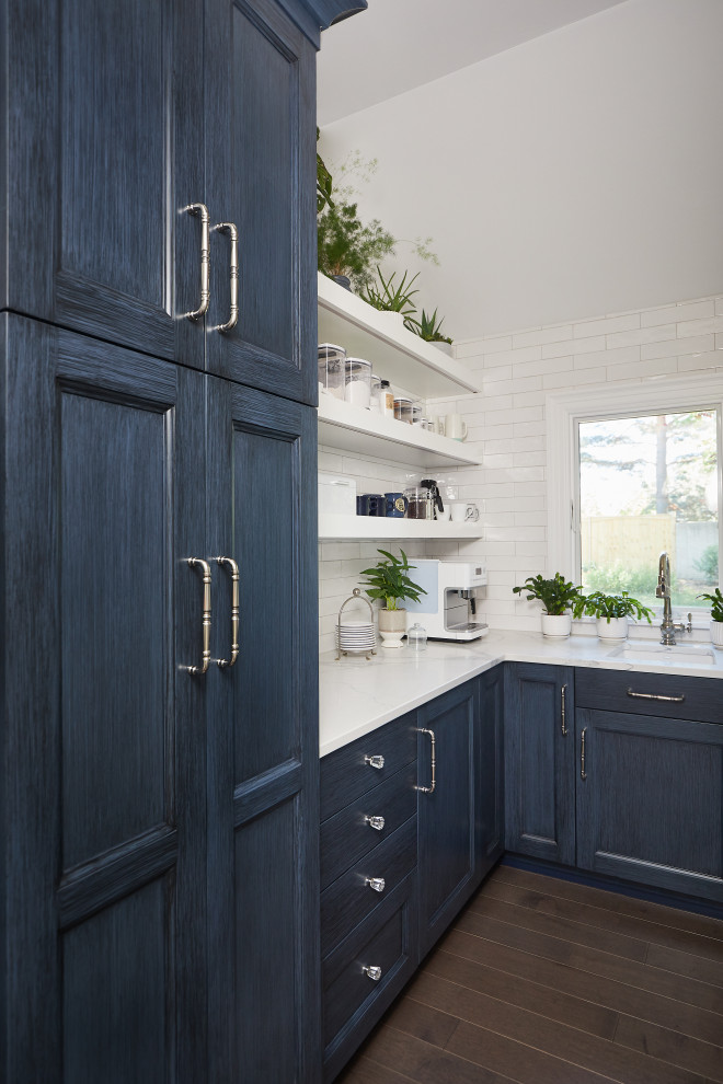 Design ideas for a large transitional l-shaped kitchen pantry in Grand Rapids with an undermount sink, recessed-panel cabinets, quartz benchtops, white splashback, dark hardwood floors, brown floor, white benchtop, blue cabinets and glass tile splashback.