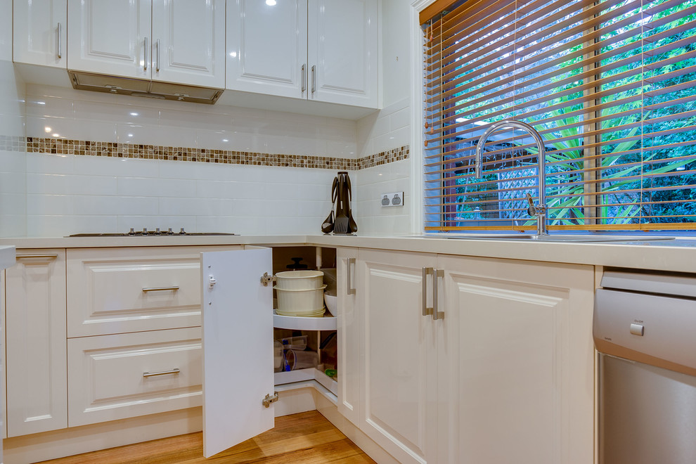 Design ideas for a large contemporary l-shaped eat-in kitchen in Melbourne with a double-bowl sink, recessed-panel cabinets, white cabinets, solid surface benchtops, white splashback, with island, subway tile splashback, stainless steel appliances and light hardwood floors.