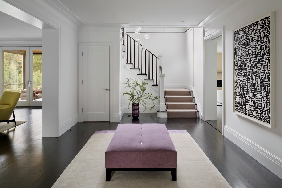 This is an example of a large transitional foyer in New York with dark hardwood floors and white walls.