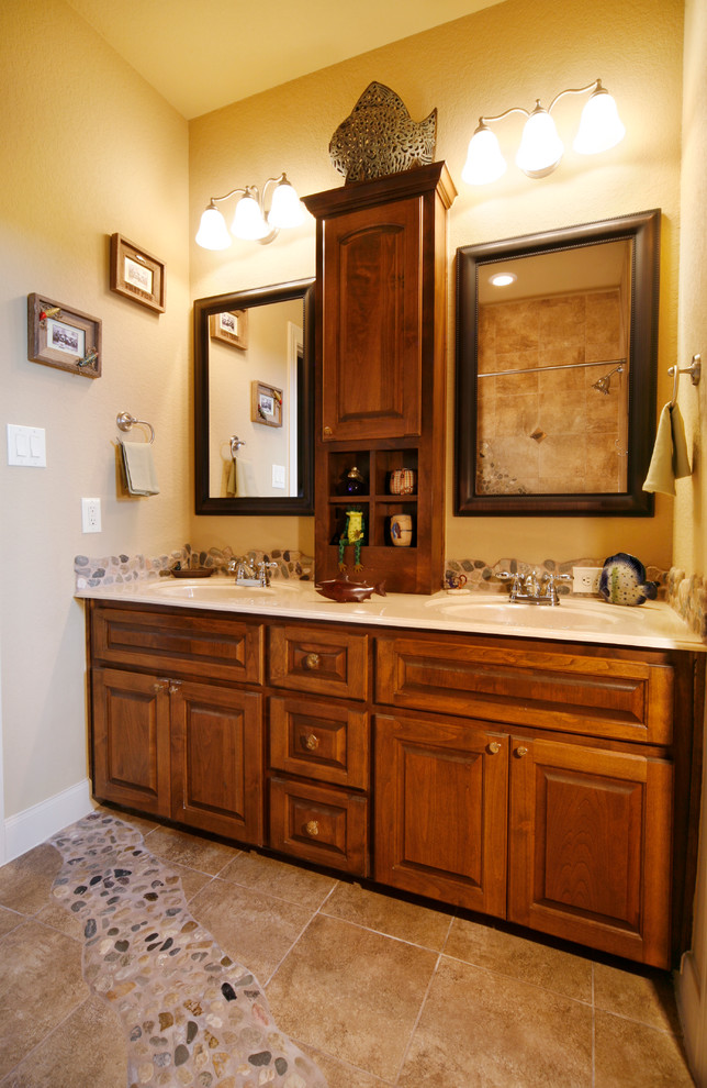Inspiration for a mid-sized traditional master bathroom in Austin with raised-panel cabinets, medium wood cabinets, pebble tile, beige walls, travertine floors, an undermount sink and solid surface benchtops.