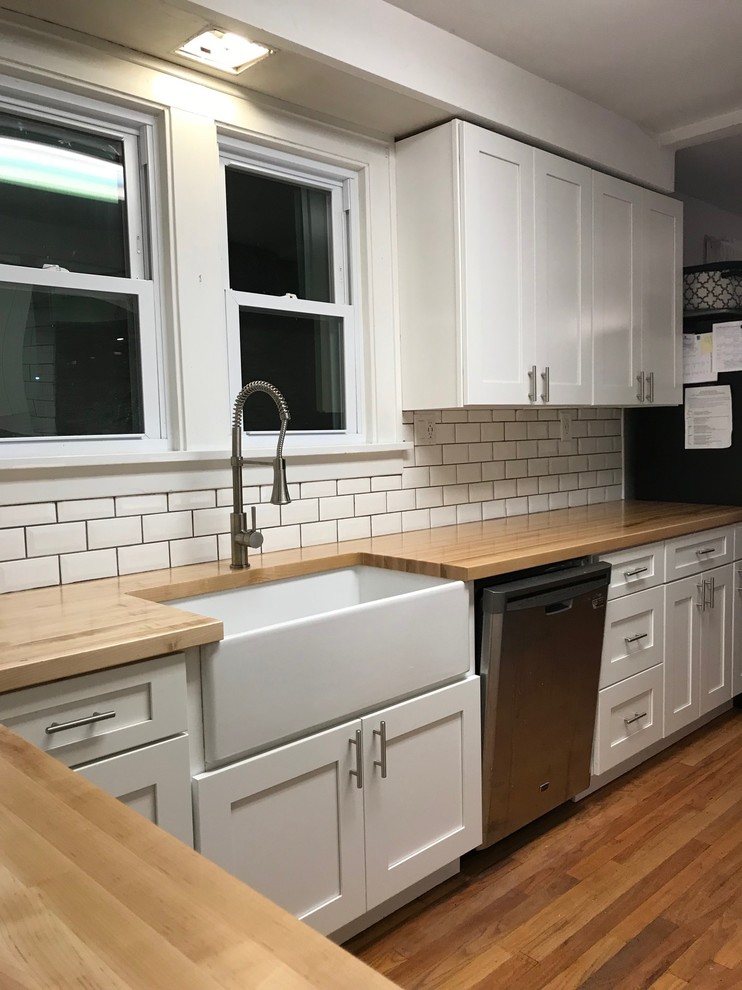 Photo of a mid-sized country galley eat-in kitchen in Orlando with a farmhouse sink, shaker cabinets, white cabinets, wood benchtops, white splashback, subway tile splashback, white appliances, medium hardwood floors, no island and yellow floor.
