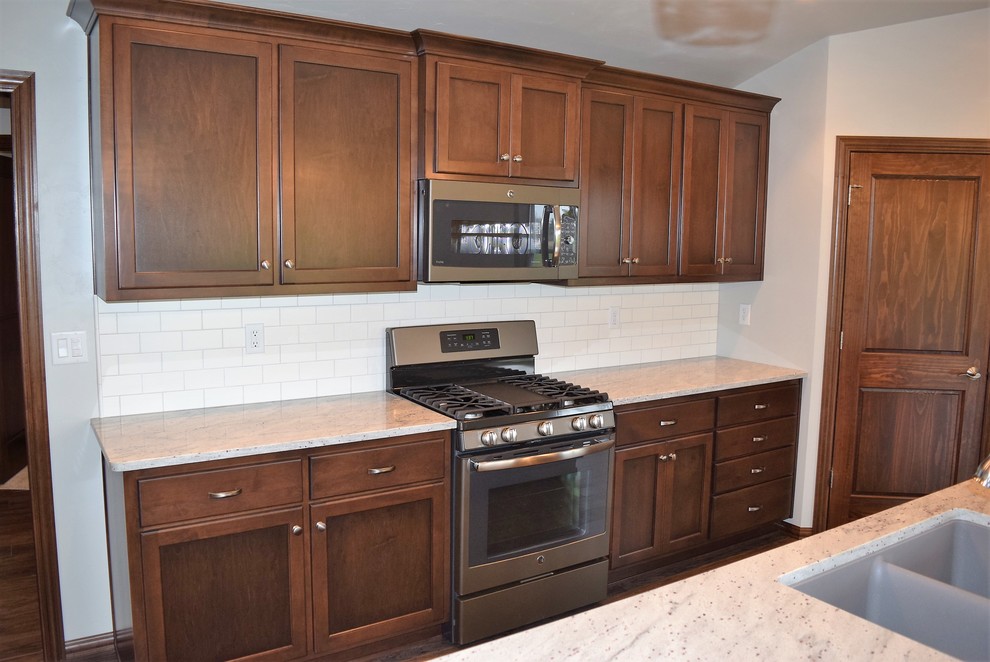 Open concept kitchen - medium tone wood floor open concept kitchen idea with an undermount sink, flat-panel cabinets, dark wood cabinets, granite countertops, white backsplash, ceramic backsplash, stainless steel appliances and an island