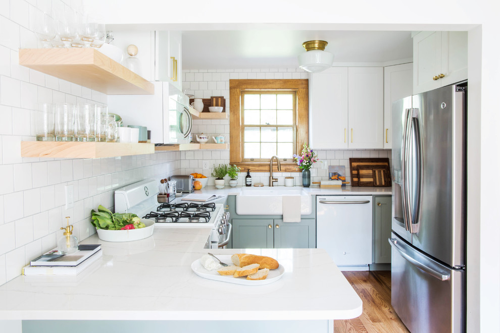 Design ideas for a small transitional u-shaped eat-in kitchen in Other with a farmhouse sink, shaker cabinets, blue cabinets, quartz benchtops, white splashback, porcelain splashback, white appliances, medium hardwood floors, a peninsula and brown floor.