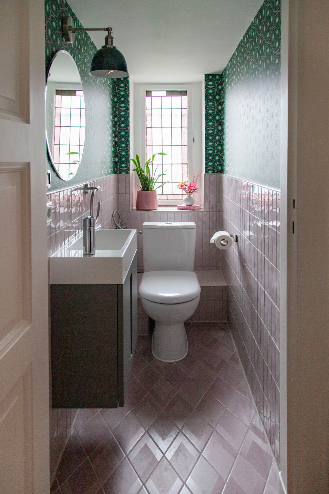 Photo of a small eclectic ensuite bathroom in Berlin with flat-panel cabinets, grey cabinets, a one-piece toilet, pink tiles, ceramic tiles, green walls, ceramic flooring, an integrated sink, laminate worktops, pink floors, white worktops, an enclosed toilet, a single sink, a floating vanity unit and wallpapered walls.