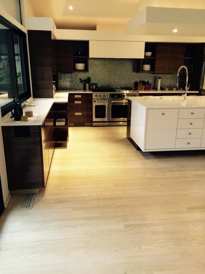 Example of a large l-shaped light wood floor open concept kitchen design in New York with an integrated sink, flat-panel cabinets, white cabinets, blue backsplash, glass sheet backsplash, stainless steel appliances and an island