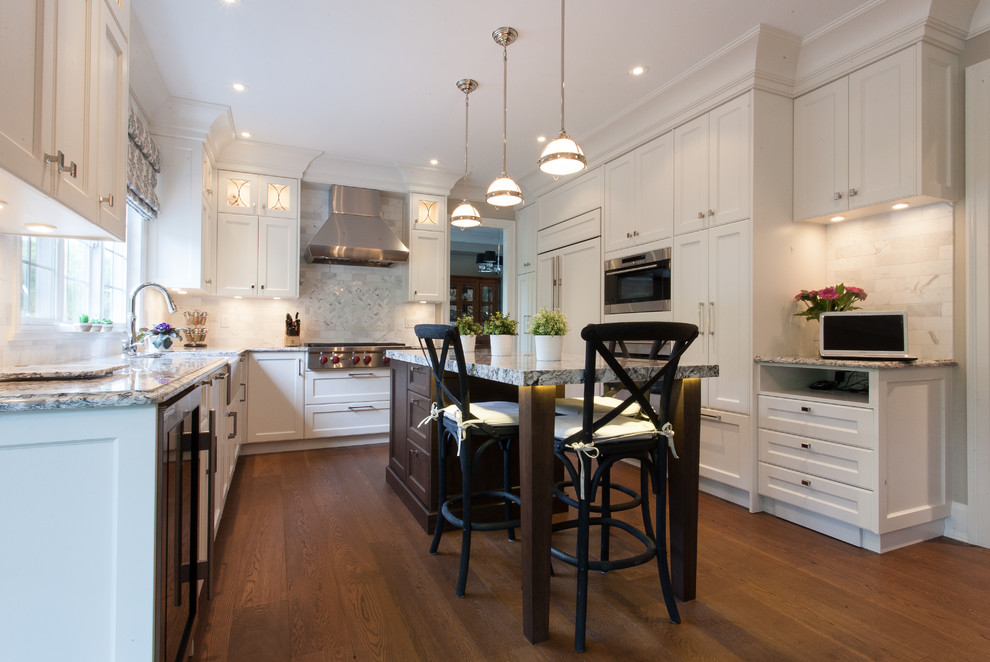 Design ideas for a large traditional u-shaped eat-in kitchen in Vancouver with a farmhouse sink, shaker cabinets, white cabinets, granite benchtops, beige splashback, stone tile splashback, panelled appliances, medium hardwood floors and with island.