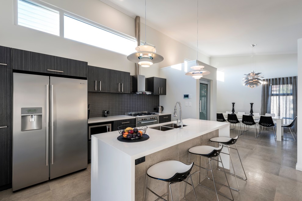 Mid-sized contemporary galley open plan kitchen in Perth with an undermount sink, flat-panel cabinets, dark wood cabinets, solid surface benchtops, ceramic splashback, stainless steel appliances, ceramic floors, with island, grey floor and black splashback.
