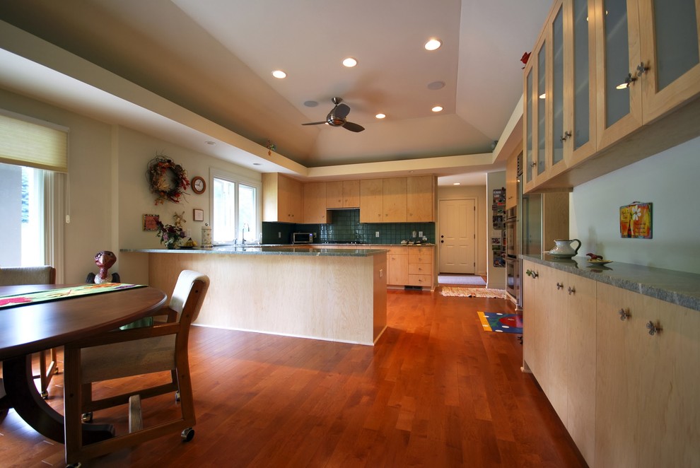 Large transitional u-shaped eat-in kitchen in Minneapolis with an undermount sink, flat-panel cabinets, light wood cabinets, granite benchtops, green splashback, glass tile splashback, stainless steel appliances, medium hardwood floors and no island.