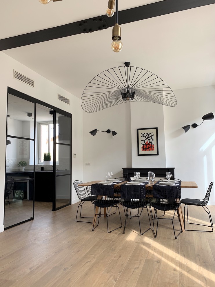 This is an example of a mid-sized contemporary open plan dining in Marseille with white walls, light hardwood floors, a standard fireplace, a plaster fireplace surround and beige floor.