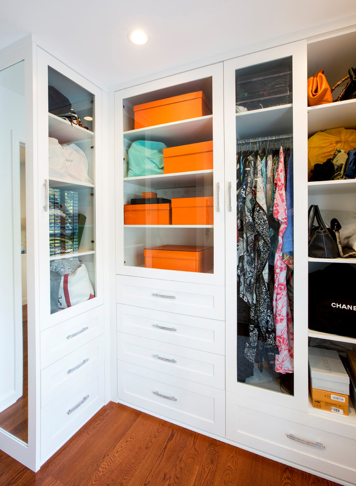 Photo of a mid-sized traditional women's walk-in wardrobe in New York with glass-front cabinets, white cabinets, medium hardwood floors and brown floor.