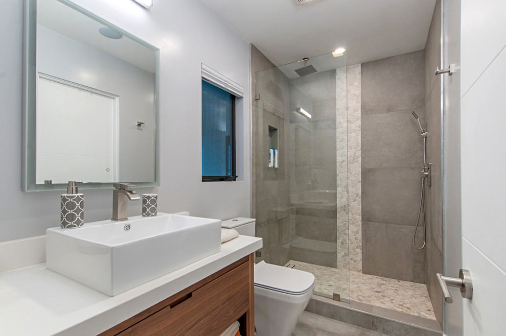 Large modern master wet room bathroom in San Diego with flat-panel cabinets, medium wood cabinets, a freestanding tub, gray tile, travertine, grey walls, cement tiles, a vessel sink, engineered quartz benchtops, grey floor and a hinged shower door.