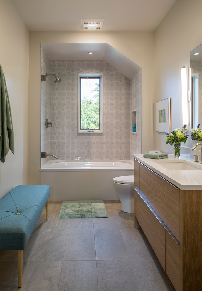 This is an example of a large transitional bathroom in Other with flat-panel cabinets, medium wood cabinets, an alcove tub, a shower/bathtub combo, a one-piece toilet, blue tile, white walls, porcelain floors, an undermount sink, grey floor, a hinged shower door and white benchtops.