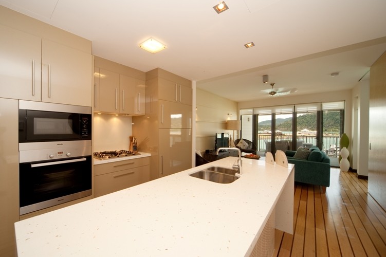 Design ideas for a beach style galley eat-in kitchen in Melbourne with an undermount sink, flat-panel cabinets, beige cabinets, laminate benchtops, white splashback, stone slab splashback, black appliances, bamboo floors and with island.