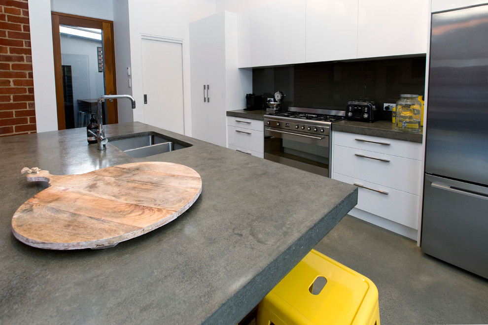 Design ideas for a mid-sized industrial galley eat-in kitchen in Adelaide with an undermount sink, flat-panel cabinets, white cabinets, concrete benchtops, grey splashback, glass sheet splashback, stainless steel appliances, concrete floors and with island.