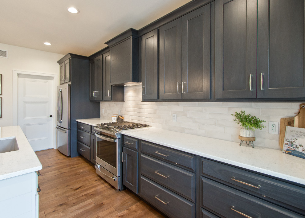 Transitional single-wall light wood floor and brown floor eat-in kitchen photo with an undermount sink, raised-panel cabinets, dark wood cabinets, quartz countertops, white backsplash, brick backsplash, stainless steel appliances, an island and white countertops
