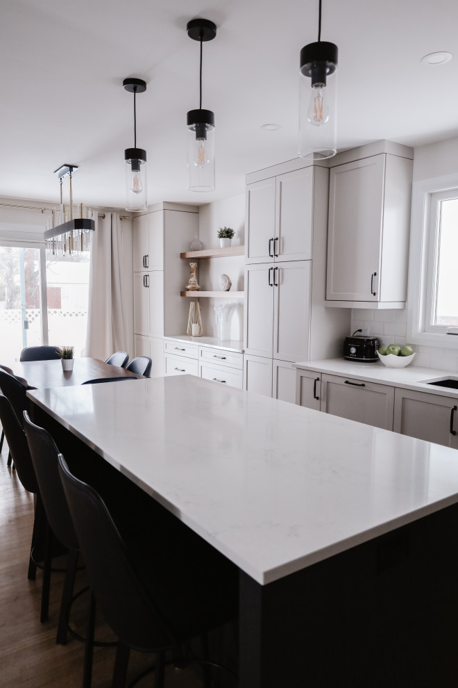 Inspiration for a mid-sized transitional l-shaped medium tone wood floor and brown floor eat-in kitchen remodel in Ottawa with an undermount sink, shaker cabinets, gray cabinets, quartz countertops, white backsplash, subway tile backsplash, stainless steel appliances, an island and white countertops