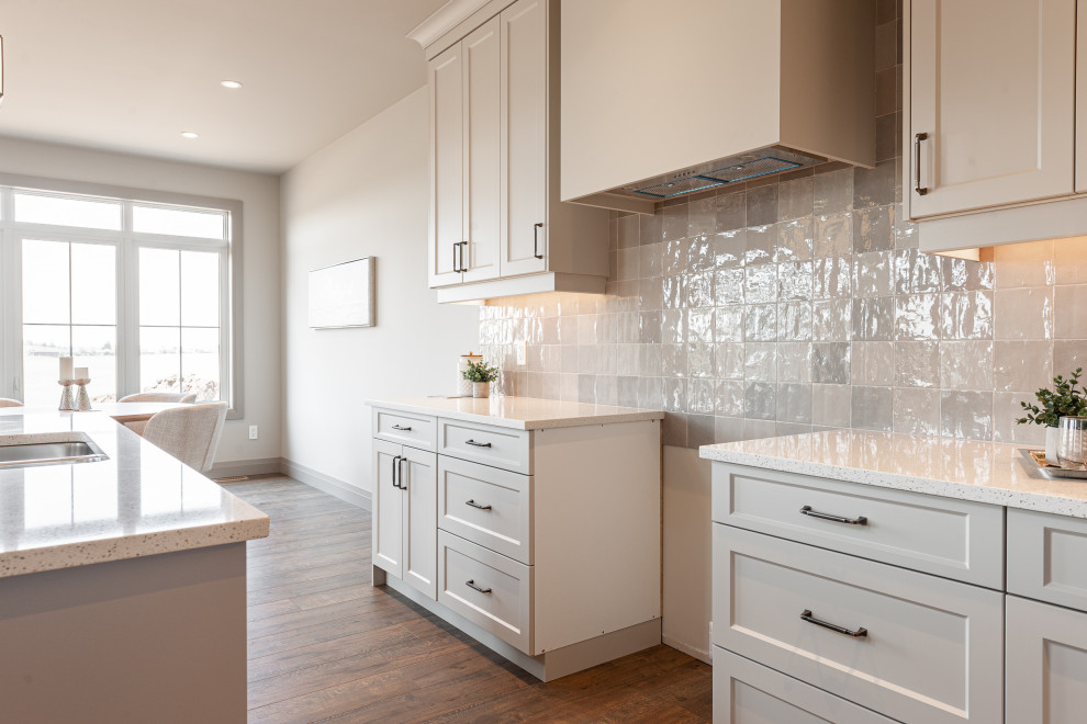 Open concept kitchen - small transitional galley laminate floor and brown floor open concept kitchen idea in Toronto with a double-bowl sink, recessed-panel cabinets, beige cabinets, quartz countertops, beige backsplash, porcelain backsplash, stainless steel appliances, an island and white countertops