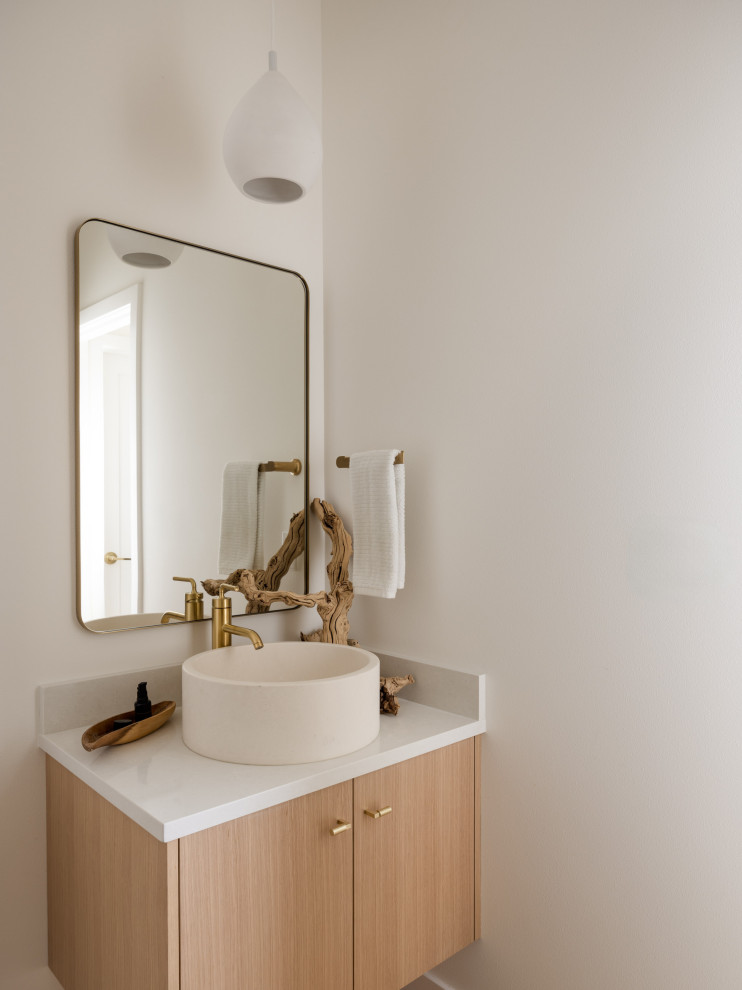 Example of a mid-sized beach style medium tone wood floor and brown floor powder room design in Seattle with flat-panel cabinets, light wood cabinets, a one-piece toilet, white walls, a vessel sink, quartzite countertops, white countertops and a floating vanity