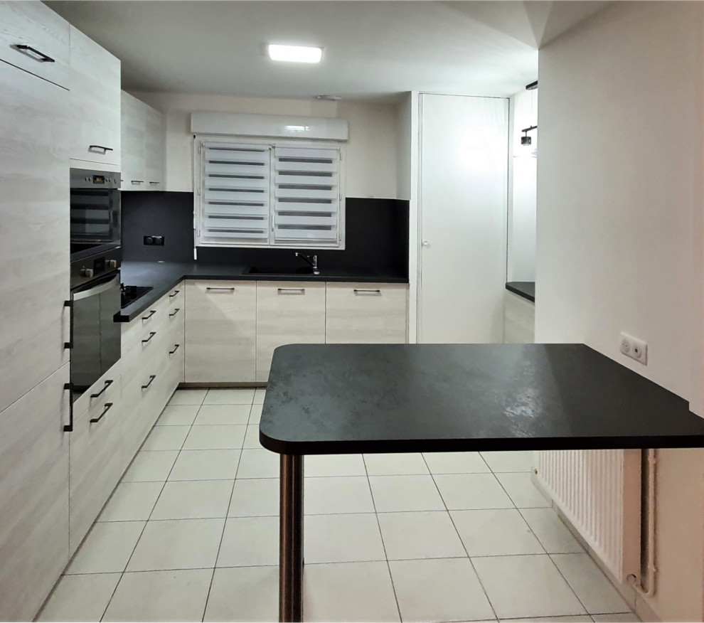 Photo of a mid-sized contemporary l-shaped open plan kitchen in Other with an undermount sink, flat-panel cabinets, stainless steel cabinets, granite benchtops, grey splashback, granite splashback, panelled appliances, cement tiles, with island, white floor and black benchtop.
