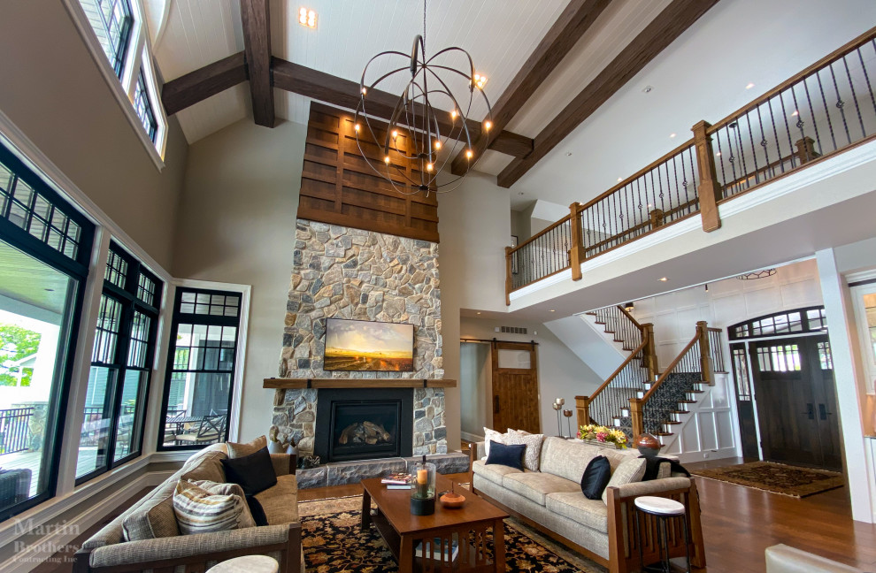 This is an example of an expansive country open concept living room in Other with beige walls, medium hardwood floors, a standard fireplace, a stone fireplace surround, a wall-mounted tv, vaulted and decorative wall panelling.