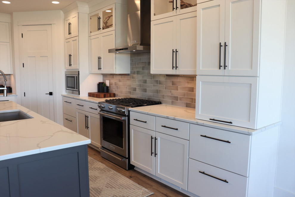 Large transitional l-shaped medium tone wood floor and brown floor open concept kitchen photo with a single-bowl sink, shaker cabinets, white cabinets, quartz countertops, gray backsplash, subway tile backsplash, stainless steel appliances, an island and white countertops