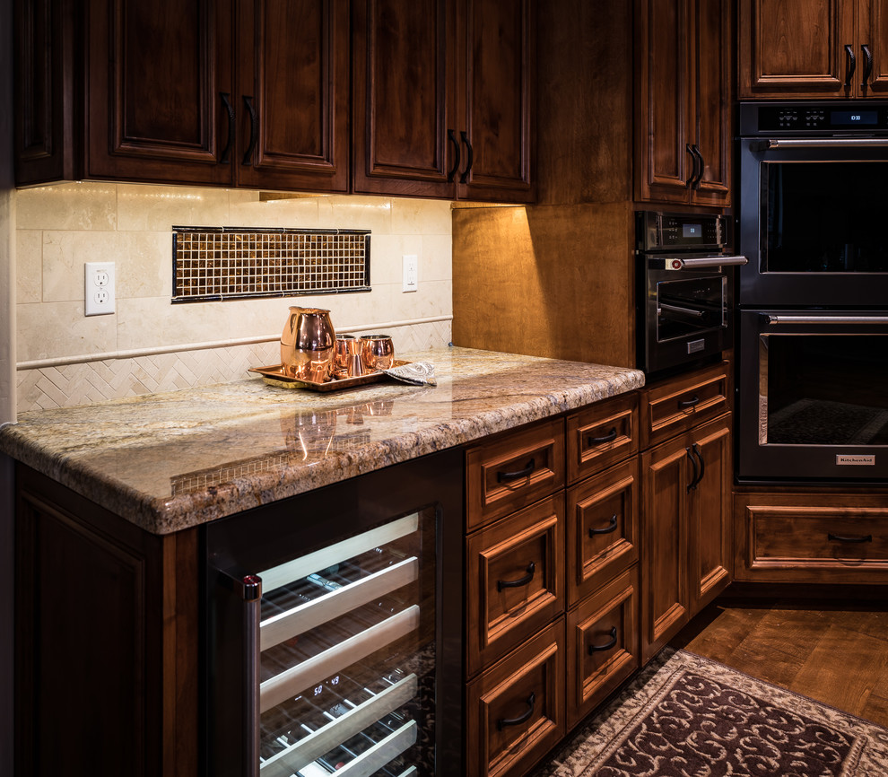 Open concept kitchen - mid-sized rustic l-shaped medium tone wood floor and brown floor open concept kitchen idea in Minneapolis with a single-bowl sink, raised-panel cabinets, medium tone wood cabinets, granite countertops, beige backsplash, stone tile backsplash, black appliances and an island