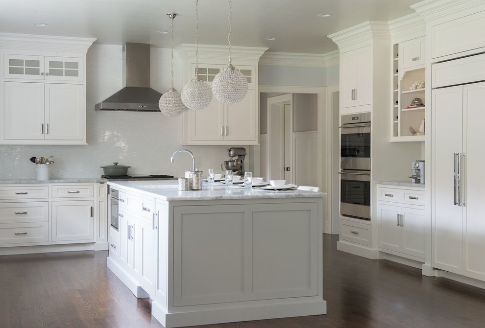 Example of a mid-sized transitional l-shaped medium tone wood floor enclosed kitchen design in DC Metro with a farmhouse sink, shaker cabinets, white cabinets, marble countertops, white backsplash, matchstick tile backsplash, an island and stainless steel appliances