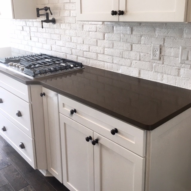 Large transitional l-shaped dark wood floor kitchen photo in Columbus with a farmhouse sink, shaker cabinets, white cabinets, quartzite countertops, white backsplash, brick backsplash, stainless steel appliances and an island