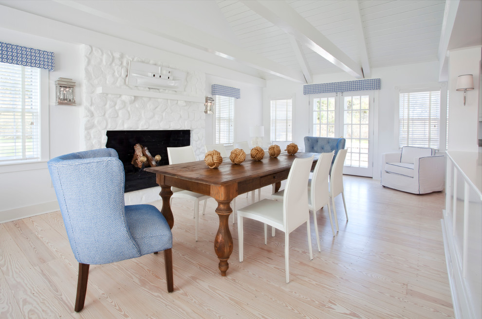 This is an example of an expansive beach style dining room in Boston with white walls, light hardwood floors, a standard fireplace and a stone fireplace surround.