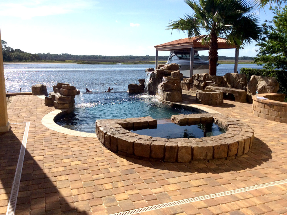 This is an example of a country backyard round infinity pool in Jacksonville with a hot tub and natural stone pavers.