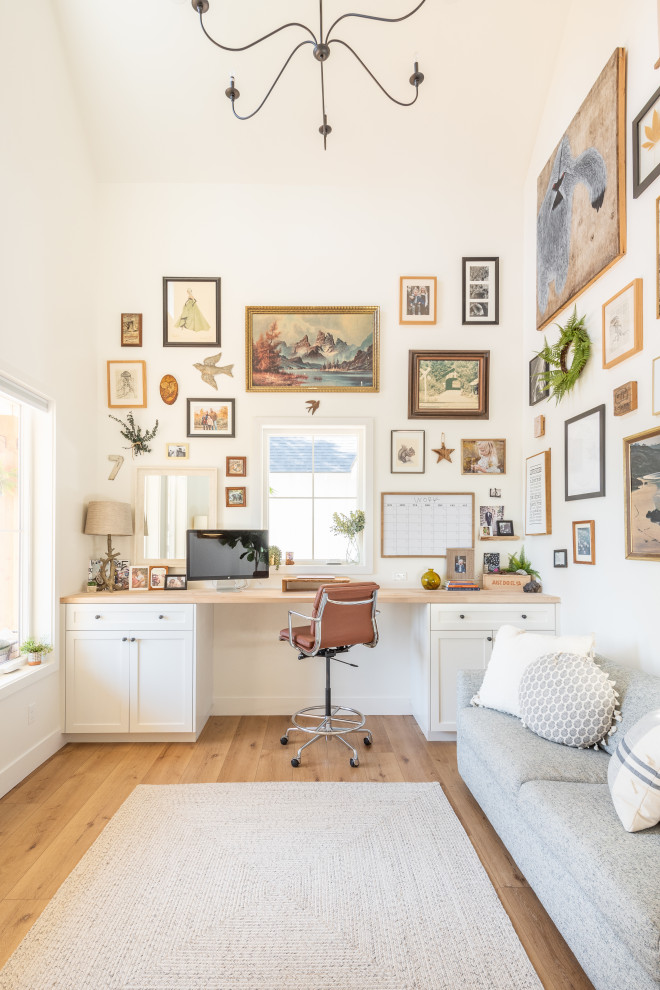 Design ideas for a farmhouse home office in Other with white walls, medium hardwood flooring, a built-in desk, brown floors and a vaulted ceiling.
