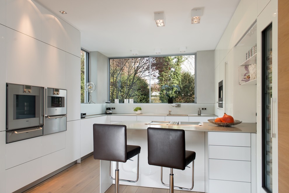 Large contemporary l-shaped separate kitchen in Munich with flat-panel cabinets, white cabinets, stainless steel appliances, medium hardwood floors, a single-bowl sink, white splashback, glass sheet splashback and a peninsula.