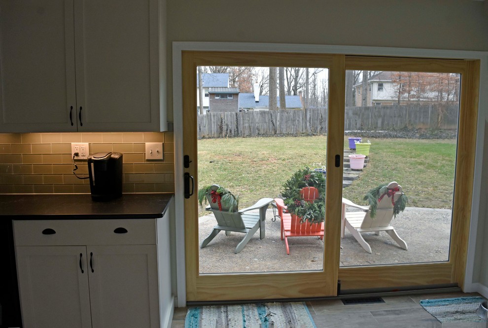 Mid-sized transitional galley laminate floor and brown floor enclosed kitchen photo in DC Metro with a farmhouse sink, shaker cabinets, white cabinets, granite countertops, gray backsplash, subway tile backsplash, stainless steel appliances, no island and black countertops