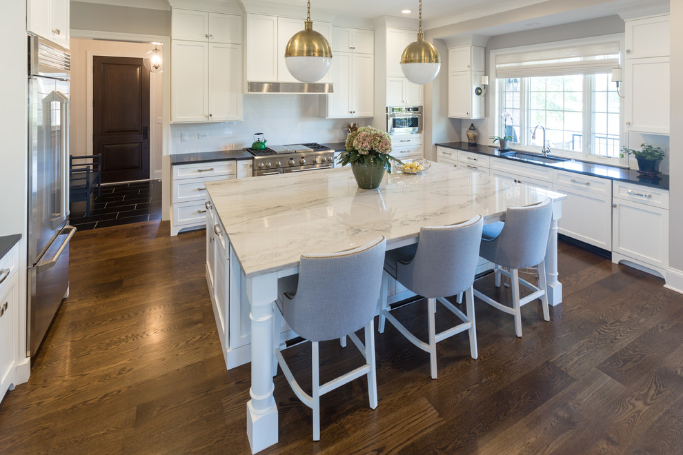 Inspiration for a large transitional u-shaped dark wood floor and brown floor kitchen remodel in Chicago with an undermount sink, shaker cabinets, white cabinets, solid surface countertops, white backsplash, ceramic backsplash, stainless steel appliances, an island and black countertops