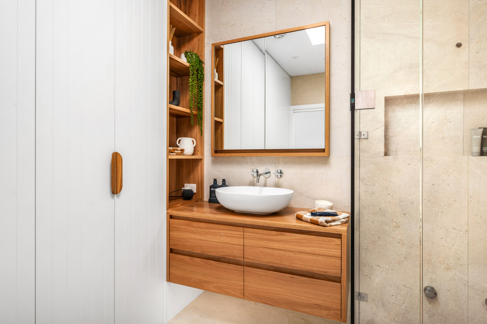 This is an example of a large beach style master bathroom in Newcastle - Maitland with flat-panel cabinets, medium wood cabinets, a corner shower, a one-piece toilet, beige tile, a vessel sink, wood benchtops, beige floor, a hinged shower door, a niche, a single vanity and a floating vanity.